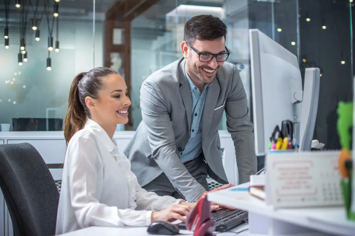 Small business owner scaling LLC from solo to team by onboarding first employee at office computer workstation