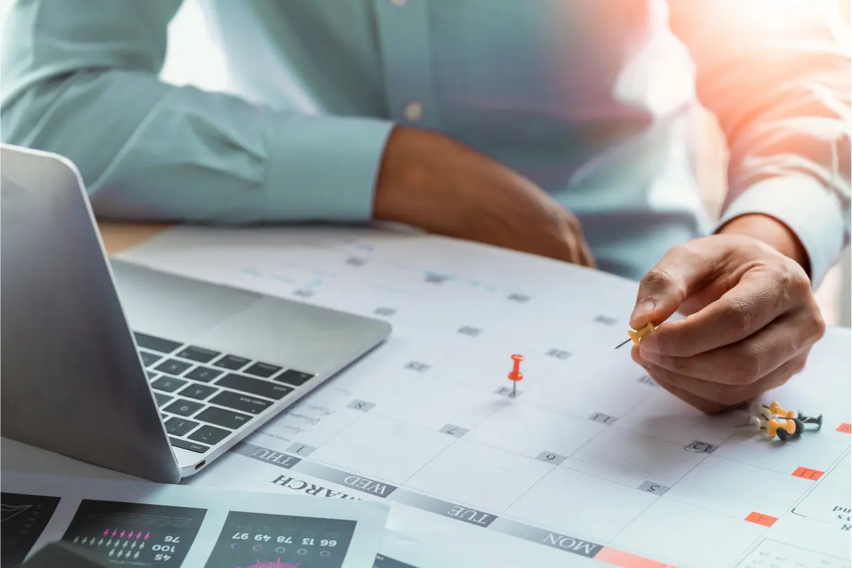 Business owner planning compliance deadlines on calendar with laptop for annual report filing and corporate compliance management.