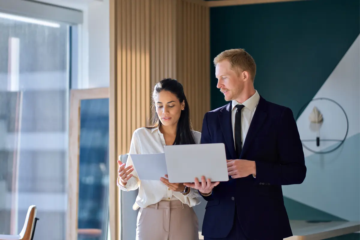 Two business consultants reviewing documents and laptop while discussing how to start a consulting business structure and legal requirements