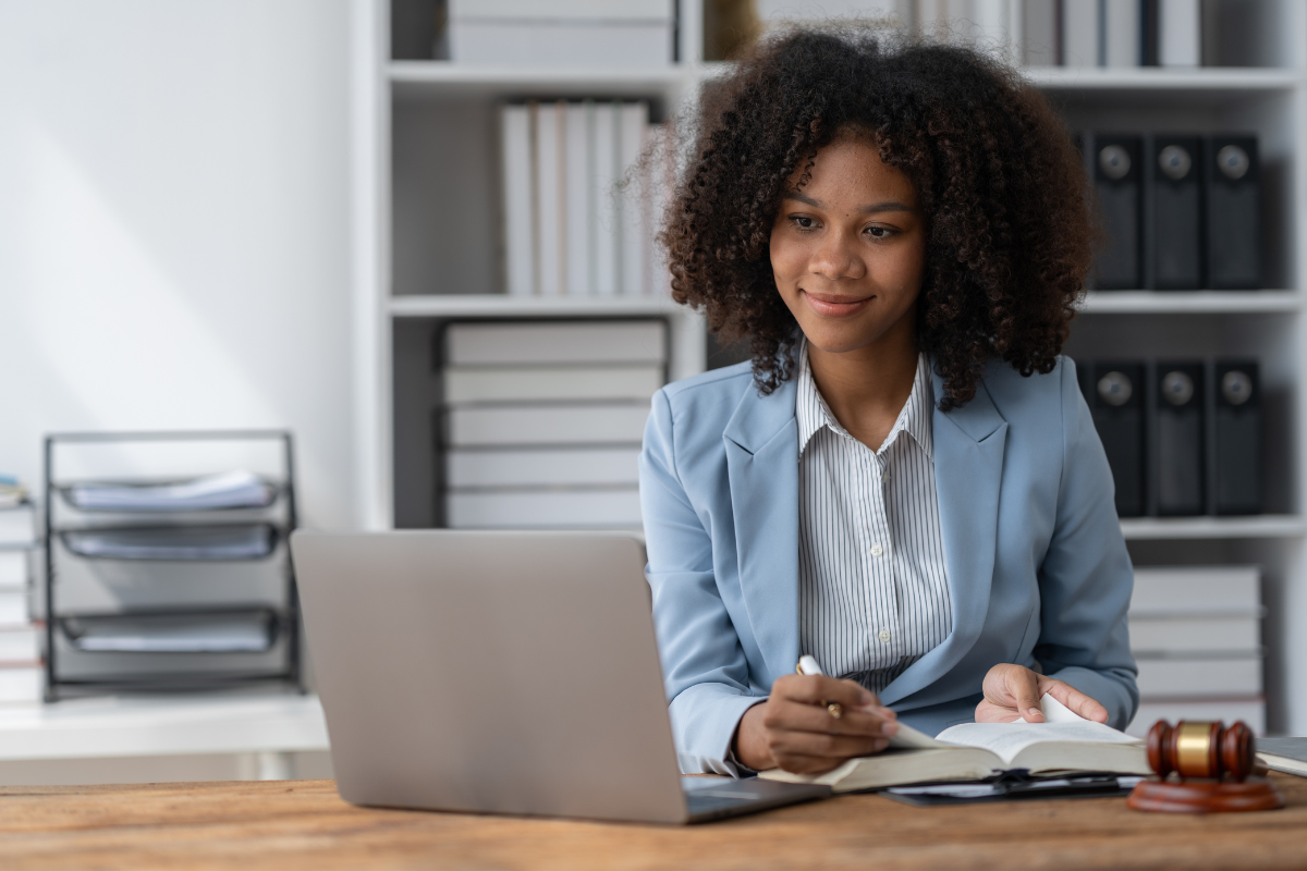 Professional woman working as a registered agent, reviewing legal documents at desk with laptop, gavel, and law books in office setting.